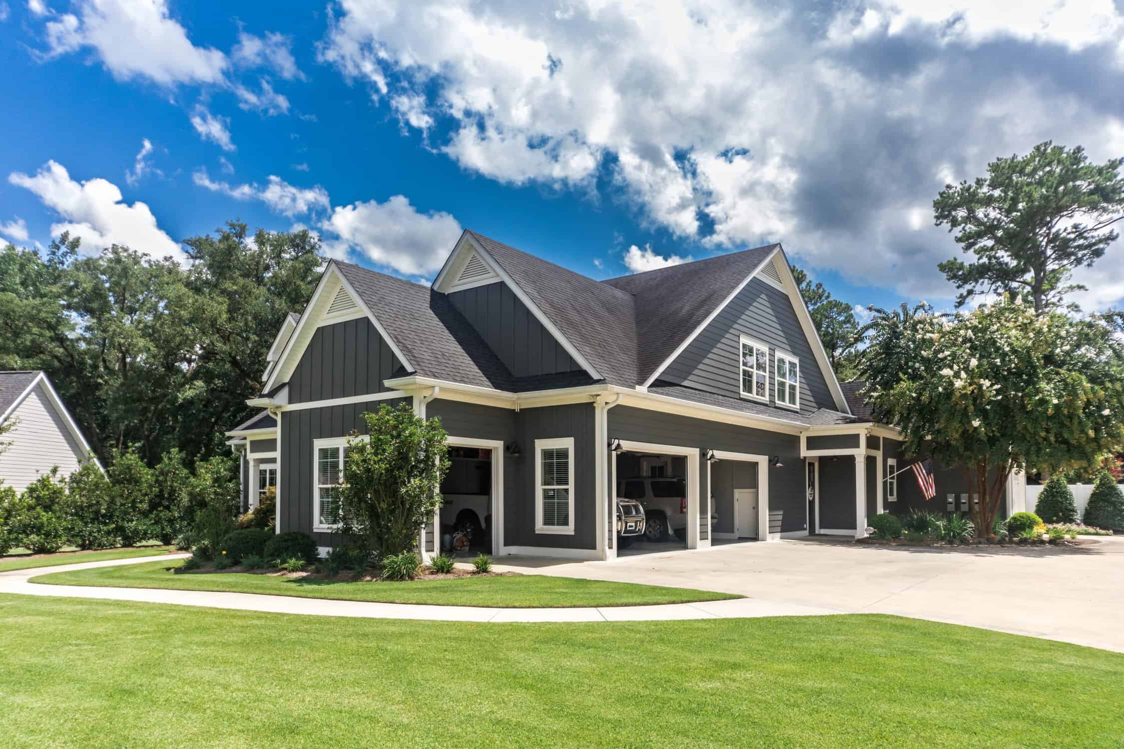 The side view of a large gray craftsman new construction house with a landscaped yard a three-car garage and driveway