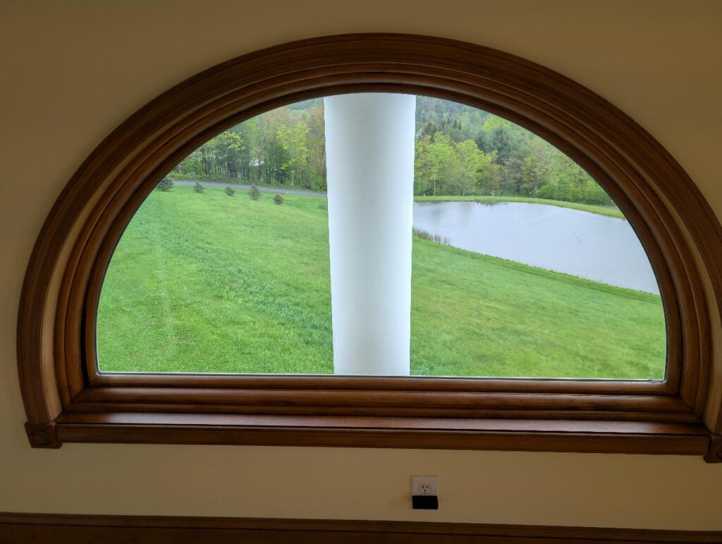 Tan-painted wall with dark wood arched window frame overlooking green lawn and pond exterior