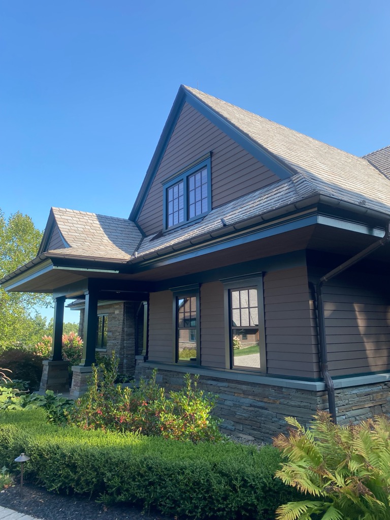 Side view of a beautifully painted house exterior featuring brown siding, dark trim, and a stone foundation.